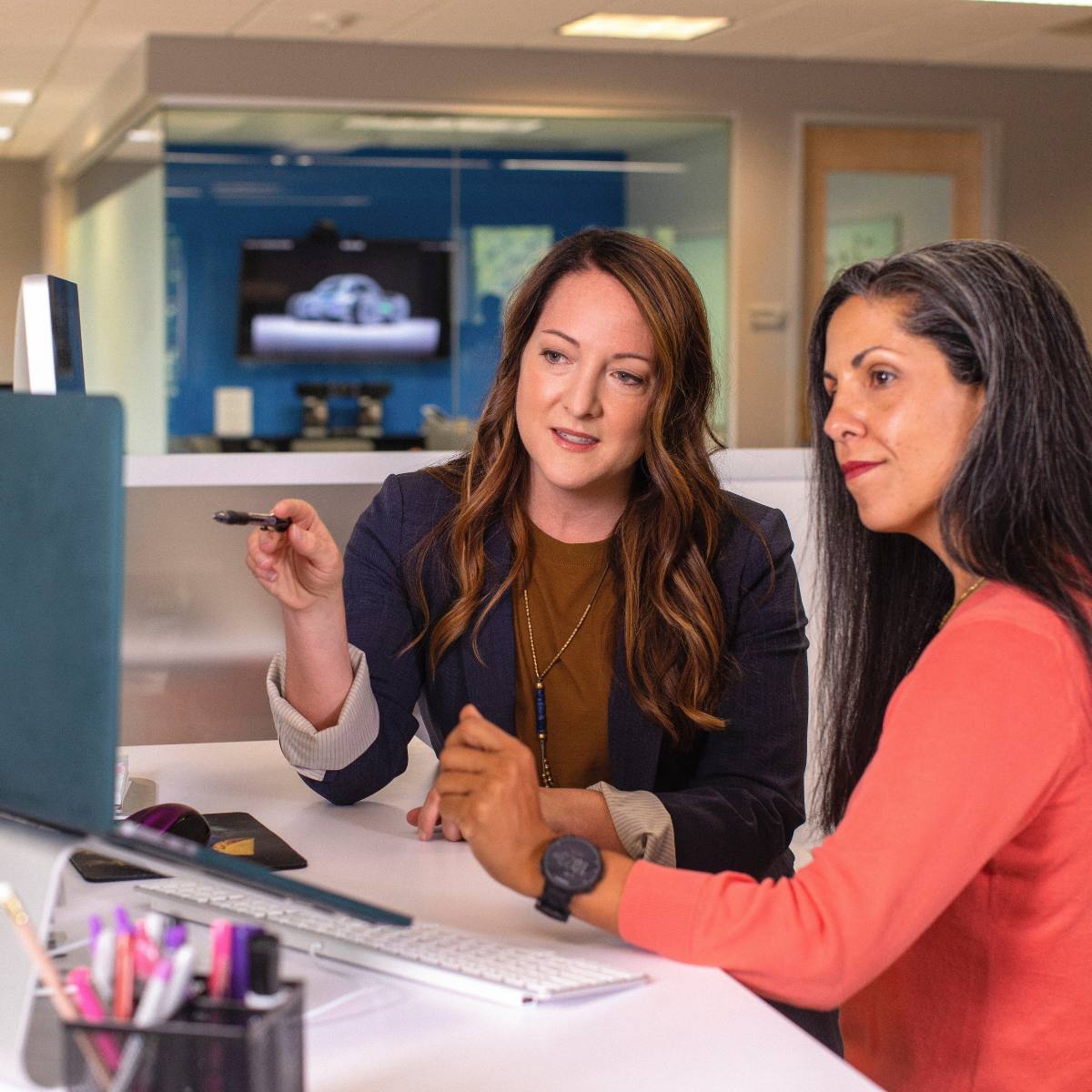 Two women working on a computer in an office space.